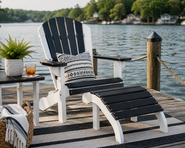 Black and white poly Adirondack chair with matching ottoman on a lakeside dock, styled with a throw pillow for relaxing waterfront views.