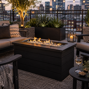Black poly fire pit creates a cozy outdoor gathering space on a modern rooftop patio with city skyline views at dusk.